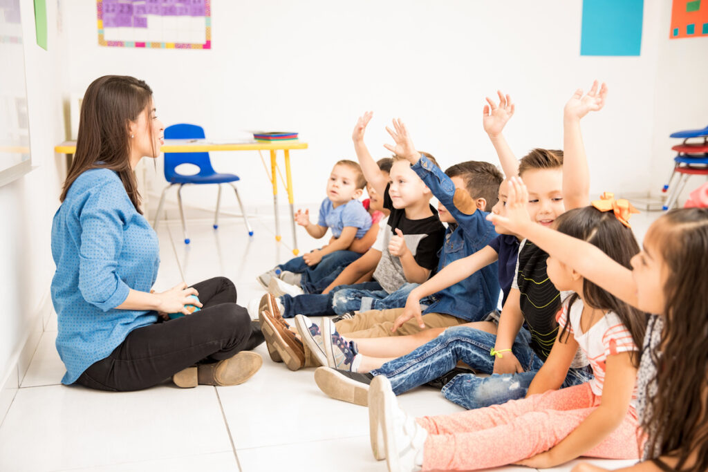 Profile view of a group of preschool students raising their hands and trying to participate at school