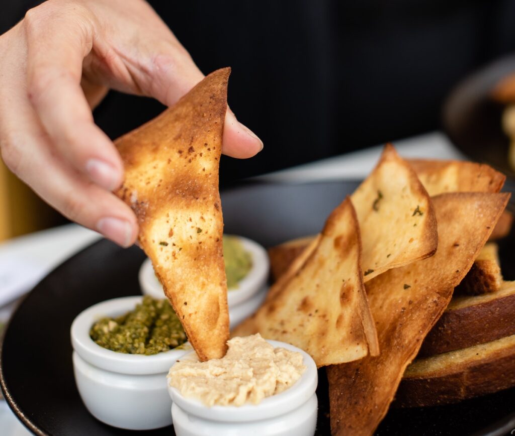 person dipping pita chip into dip