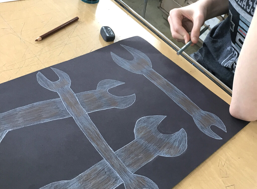 student drawing wrenches with colored pencil on black paper