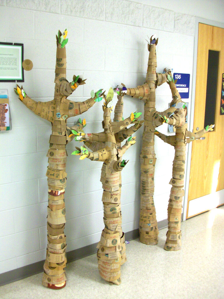 four tall trees made of coffee sleeve cardboard pieces in school hallway