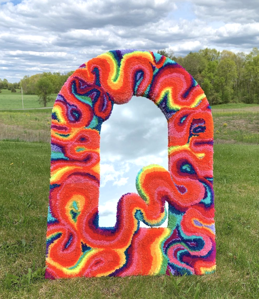 mirror with swirling rainbow border with grass and sky background