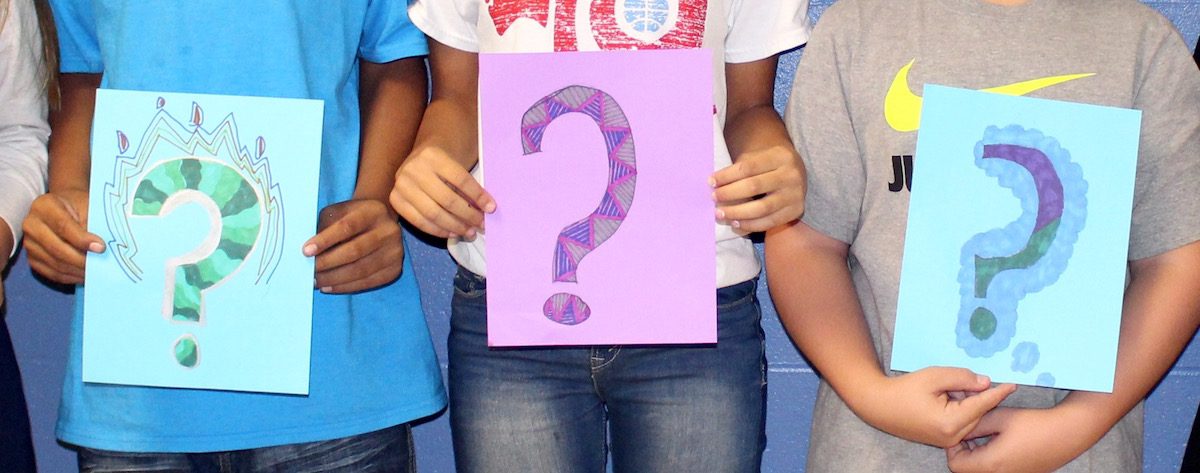 three students holding question signs