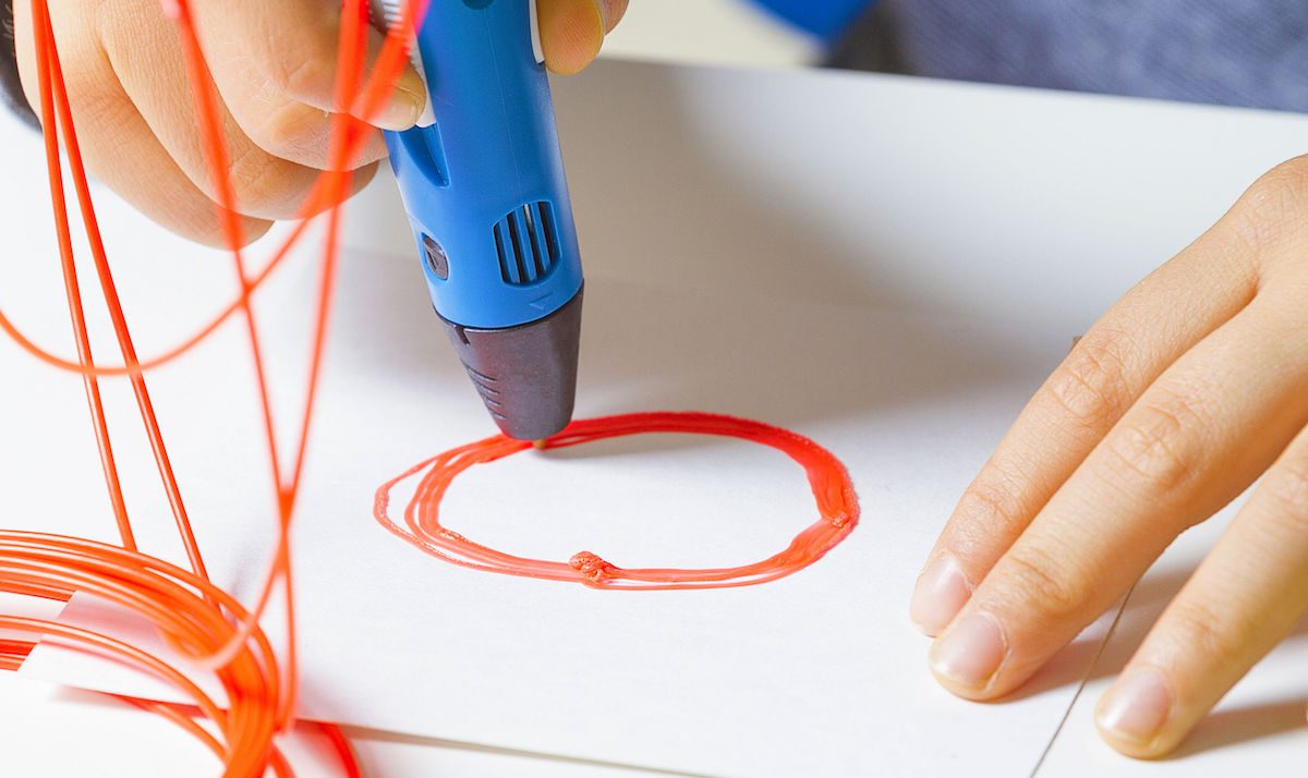 Kid hands with 3d printing pen, colorful filaments on white desk