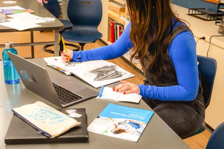 teacher drawing in a classroom with a laptop and degree program brochure
