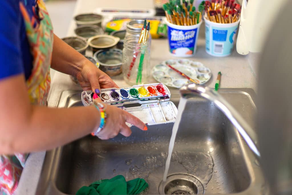 teacher cleaning watercolor palettes at the sink
