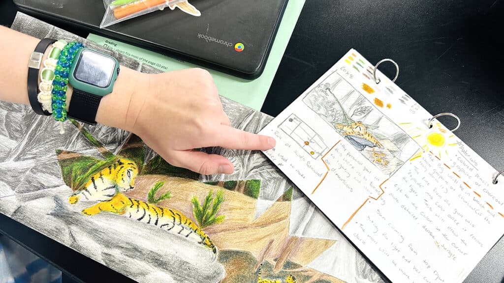 hand pointing to a sketchbook with final artwork