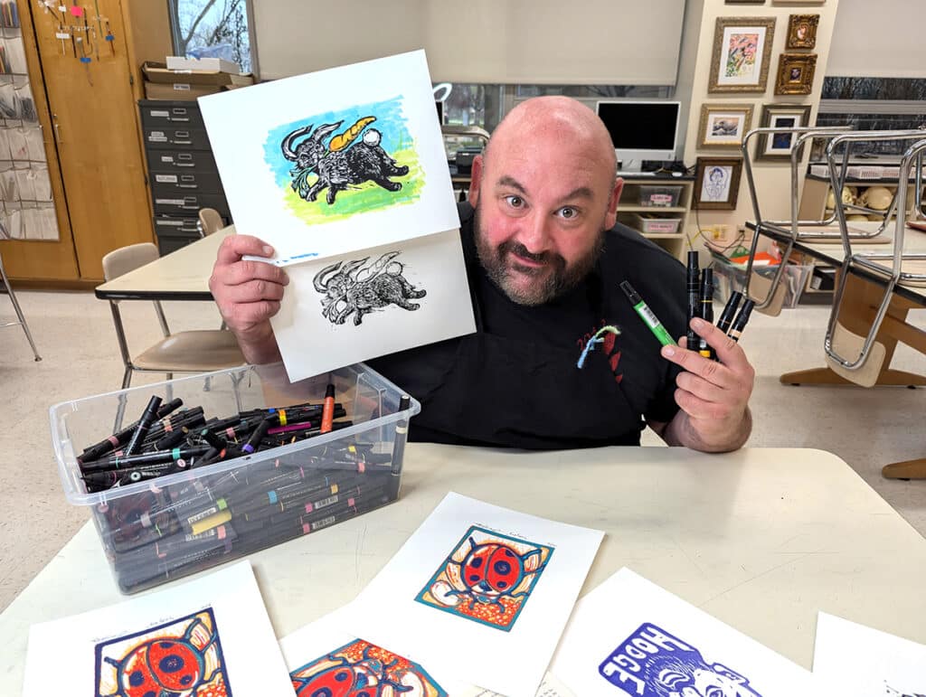 teacher holding two prints and art supplies