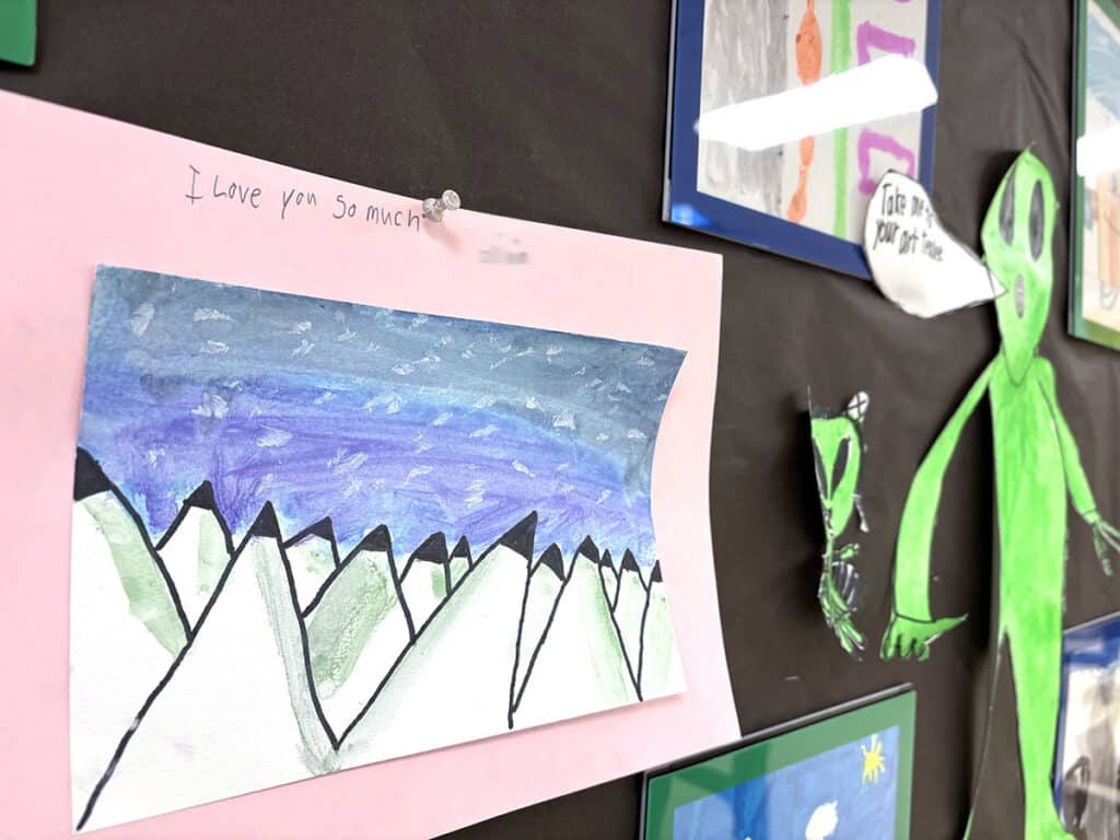 student artwork pinned on the wall with a note to the teacher