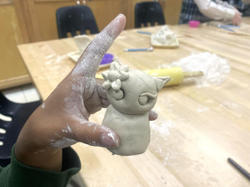 student hand holding air-dry clay creature
